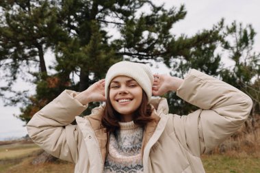 Açık havada gülümseyen bir kadın portresi, bej ceket ve rahat bir bere, sıradan moda ve kendine güvenen bir hava sergiliyor..