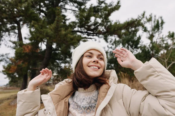 Açık havada bej ceketli ve kışlık ceketli gülümseyen bir kadın olarak sağlıklı, ışıl ışıl ve neşeli bir ifade. Günlük moda havası, doğal arka plan, samimi bir an ve açık hava yaşam tarzı.