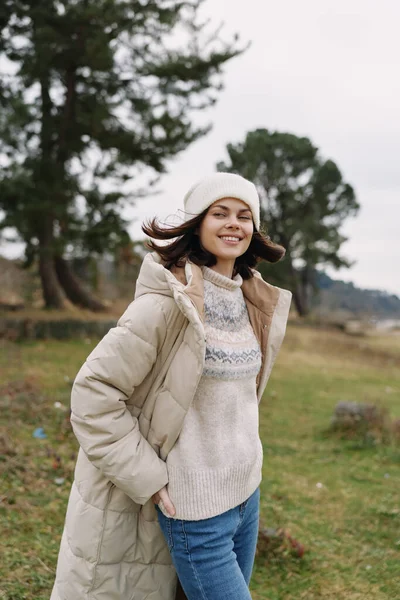 Yastıklı bir ceket ve açık havada rahat bir süveter giyen gülümseyen kadın, esinti ve yeşillikle dolu bir parkta poz veriyor, rahat bir stil yakalıyor, sıcaklığı ve samimi bir hayat tarzında doğal gün ışığını yakalıyor..