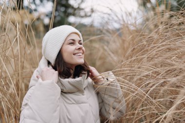 Doğal çimen tarlasında sıcacık bir palto giymiş, gülümseyen ve rahat bir kadın portresi, açık hava yaşam tarzı, konfor ve tarzını gün ışığında sergiliyor.
