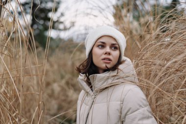 Uzun otların, dingin manzaranın, soğuk havanın, doğal ortamın ve samimi havanın ortasında kalın bir palto ve bere giyen bir kadının açık hava portresi..