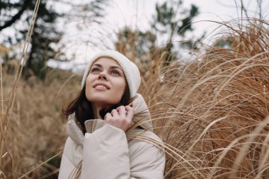 Kurumuş otların arasında, sıcak giyimli, sakin, harika ve mevsimsel bir ruh hali taşıyan bir kadının açık hava portresi. Hafif bir esinti ve sessiz bir arkaplan huzur verici, umut verici bir sahne yaratır.