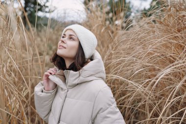 Kuru otların arasında bej ceketli ve bereli bir kadın portresi, sakin bir hava, kış havası ve açık havada yalnızlık veriyor..