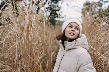 Uzun otların arasında bej rengi bir palto giyen bir kadının portresi, dingin ruh hali, doğa, soğuk hava ve açık havada sessiz tonlarla moda yakalanıyor.