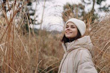 Sıcak bir palto ve bereyle gülümseyen bir kadının portresi. Kış tarlasında uzun otların arasında, sakin bir açık hava modasını ve doğayı yakalıyor.