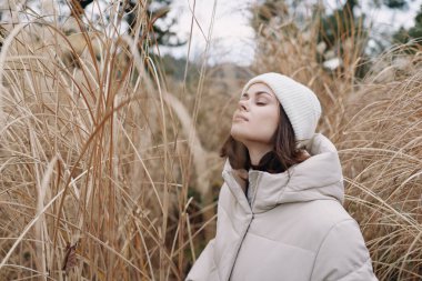 Uzun otların arasında paltosu ve beresi olan bir kadının açık hava portresi sakin bir kış havası yakalamış ve sakin bir doğa sahnesi yakalamış..