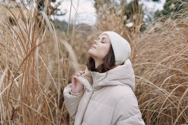 Kışın açık havada çekilmiş bir kadın portresi otların ve sazlıkların arasında takılıyor, sakin ve düşünceli, gösterişli doğa, soğuk hava havası ve rahat bir ortam.