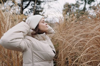 Kabarık ceketli bir kadın portresi ve çayırların arasında örgü bir şapka serin hava ve doğa sahnesinde dingin bir ruh hali..