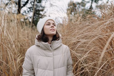 Açık havada karlı bir gün, sıcak bir ceketle şık bir kadın bej çimlerin arasında dikiliyor, gözler hafif bir ışık sükunet ve sakinliği arttırıyor..