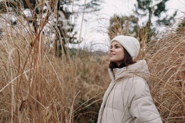Tarafsız bir ceket ve bereyle uzun otların arasında sakin doğayı ve mevsimsel sakinliği yakalayan bir kadının açık hava portresi. Moda, yaşam tarzı ve seyahat stoku görselleri için ideal.