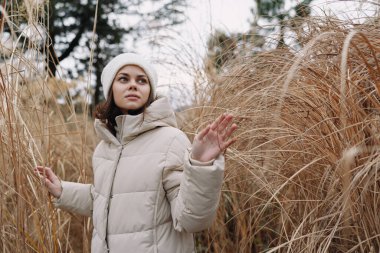 Kurumuş sazlıkların, huzurlu havanın, moda odaklı pozun, soğuk havalarda samimi bir anın, doğadan esinlenilen bir kadının olduğu açık hava sahnesi.