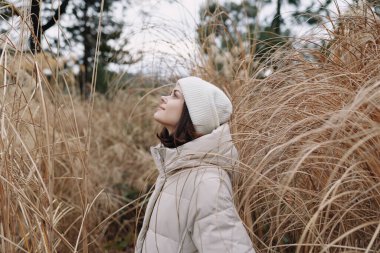 Açık hava portresi, rahat bir palto ve bereyle sonbahar otlarının arasında huzur, yalnızlık ve doğayla nazik bir bağ taşıyan bir kadın..