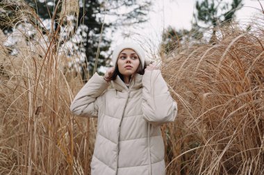 Vahşi otların arasında kalın bir palto giyen bir kadının açık hava portresi, sakin havayı, sokak stilini ve şafak vakti sakin kış atmosferini yakalıyor..