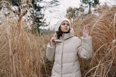 Tarafsız bir ceket ve şapkayla gezen bir kadının açık hava portresi, sakin kırsal manzarayı ileri moda ve doğal yayın havasıyla yakalıyor..