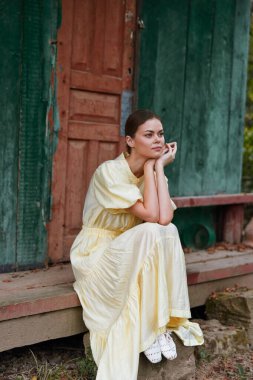 Düşünceli kadın bakıcı soluk sarı elbiseli, köy merdivenlerinde oyulmuş kapıların yanında, sakin bir anın ve huzurlu bir ruh halinin tadını çıkarıyor..