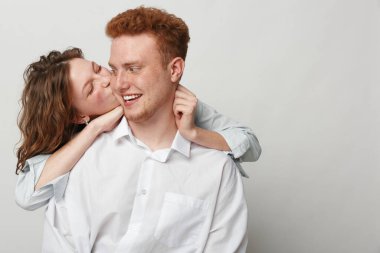 Gündelik giysiler içinde gülümseyen genç çift aşkı ve neşeyi ifade eder, kadın erkeği arkadan kucaklar ve yanağından öper. Romantizm, şefkat, bağlantı ve olumlu duygular kavramı.