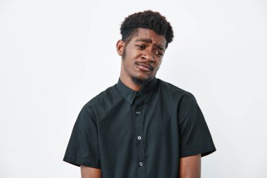 Kafası karışmış, siyah tenli, kısa kollu siyah bir adam beyaz arka planda duruyor. Stüdyo resminde şüphe veya şüphecilik gösteren afro saçlı bir erkek model..