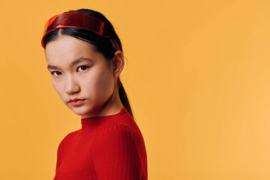 Kırmızı saç bandı takan ve aynı kırmızı gömleği giyen kadın doğrudan kameraya bakıyor. Stüdyo portresi, moda, güzellik ve kendine güvenen turuncu arkaplan.