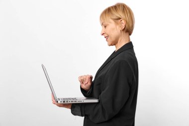 Siyah ceket giyen, dizüstü bilgisayar kullanan, beyaz arka planda duran orta yaşlı mutlu bir kadın. Dijital iletişim, uzaktan çalışma, teknoloji ve iş yaşam tarzı kavramı.