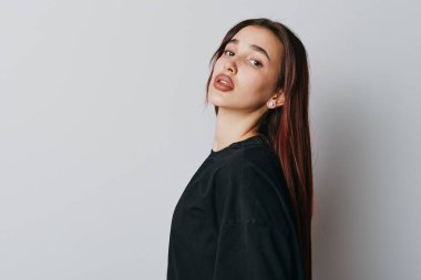 Kahverengi saçlı, sıradan siyah saçlı, beyaz arka planda duran, rahat duruş sergileyen ve moda veya güzellik anlayışı için minimalist tarzda ince makyaj yapan bir kadın model..