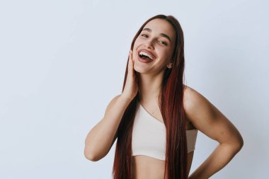 Uzun düz saçlı, sıradan kıyafetli, gülümseyen genç bir kadın yanağına dokundu. Neşeli duyguları olan ve sağlık, sağlık veya moda teması için temiz geçmişi olan kadın portresi.