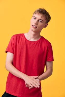 Kırmızı tişörtlü sıradan bir erkek model, cesur sarı bir arka planda, yaklaşılabilir stil, gençlik enerjisi ve modern moda, yaşam tarzı markalaşması ve pazarlama için ideal dostane bir ruh hali içinde poz veriyor.
