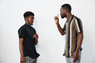 Esmer tenli Afro-Amerikalı erkekler odaklanmış ifadelerle tartışıyorlar. Sıradan kıyafet, beyaz arka planda durmak, bir adam el hareketleriyle açıklama yapıyor, diğeri dinliyor..