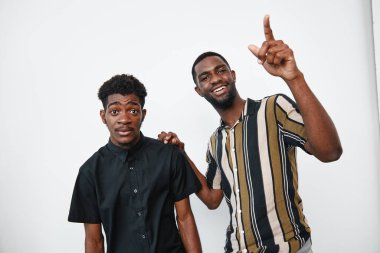 Siyah tenli Afrikalı erkekler beyaz arka planda poz veriyor. Biri yukarı bakıyor ve gülümsüyor. Diğeri ise stüdyo ortamında çizgili ve siyah gömlekler giyiyor..