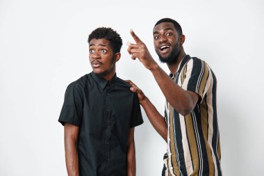 Siyah tenli, sıradan tişörtlü Afro-Amerikalı erkekler, biri heyecanlı bir şekilde ve diğeri de şaşkın görünüyor, beyaz arka planda duygusal ifadeler ve etkileşimle izole edilmiş..