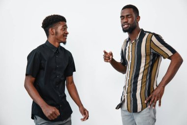 Esmer tenli Afro-Amerikalı erkekler günlük gömlekler giyip stüdyoda dikiliyor ve etkileşime giriyorlar. İki genç erkek arkadaş sohbet ediyor ve birlikte eğleniyorlar..