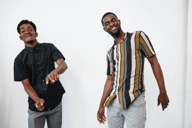 Siyah tenli, sıradan gömlekler giyen ve kot pantolon giyen iki siyah adam mutlu bir şekilde dans ediyor. Dostlar neşe ve dostluğu gülümseme ve hareketle ifade ederler..