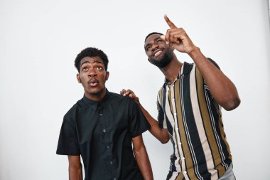 Siyah tenli, üstü açık tişörtlü Afro-Amerikalı erkekler. Biri yukarıya bakıyor. Diğeri ise beyaz duvar arkaplanlı stüdyoda şaşkınlık, dostluk ve iletişim gösteriyor..