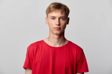 Parlak kırmızı tişörtlü genç erkek, basit bir stüdyo ortamında poz verdi, ekommerce ve editoryal kullanım için minimal bir moda çekimi sergiliyor, gündelik kıyafetleri, modern tasarımı ve yeni bir günlük resmi vurguluyor.