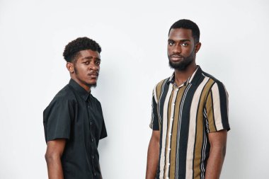 Siyah tenli, beyaz arka planda yan yana duran, tarafsız ifadeleri ve rahat duruşu olan iki Afro-Amerikalı adamın portresi..