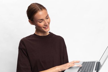 Koyu renk tişörtlü, sırıtan kadın elinde dizüstü bilgisayarla ekrana bakıyor. Beyaz arka planda izole edilmiş. Teknoloji kullanımı, iletişim ve günlük dijital yaşam tarzı kavramı.