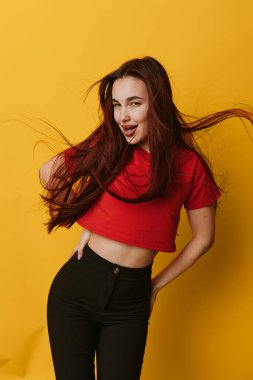 Kırmızı gömlekli, siyah pantolonlu ve sarı arka planda duran genç kadın modelin portresi. Şık, modaya uygun, kendine güvenen, eğlenceli ve dinamik pozlar veren doğal görünüşlü bir kadın..