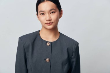 Profesyonel iş profili ya da şirket portresi için arka planda tarafsız yüz ifadesi olan koyu renk ceket giyen kendine güvenen genç Asyalı kadın..