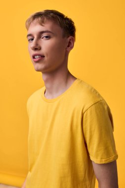 Sıcak bir arka plan, temiz bir kompozisyon, stüdyo ışıklandırması, reklamlar için çok yönlü, sosyal medya ve web sitesi kampanyalarına karşı sarı tişörtlü genç bir erkek mankenin yer aldığı sıradan bir moda çekimi..