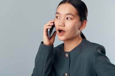 Telefonda koyu renk ceket giyen Asyalı iş kadını şok etkisi gösteriyor. İletişim, sohbet, sohbet ya da önemli haber alımı için akıllı telefonu olan genç bir kadının portresi.