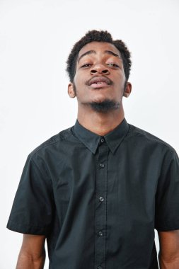 Siyah gömlekli, koyu tenli, kendine güvenen genç bir adamın portresi. Beyaz arka planda, doğal afro saçlı ve sakallı poz veriyor..