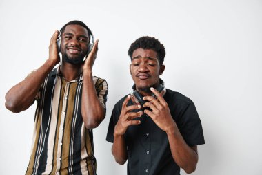 Siyah tenli genç adamlar kulaklıkla müzik dinliyorlar, zevk ve duygu gösteriyorlar, günlük gömlekler giyiyorlar, beyaz arka planda izole edilmişler..