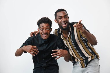 İki koyu tenli, sıradan gömlekli siyah adam beyaz arka planda gülüyor ve gülümsüyor. Arkadaşlık, neşe ve pozitif duygular. Stüdyo resminde rahat pozlarla çekilmiştir..