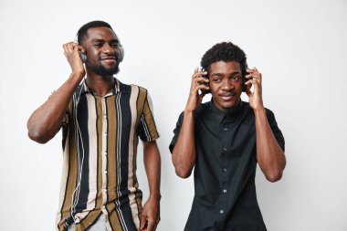 Koyu tenli, kulaklık takan ve müzik dinleyen genç siyahi erkekler. Arkadaşlar, eğlence, yaşam tarzı ve teknoloji kavramı beyaz arka plan ve pozitif ruh hali.