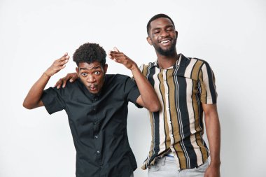 Koyu tenli genç siyahi erkekler birbirine yakın duruyor. Biri neşeli bir jest yapıyor. Sıradan bir tarz, mutlu bir ifade, arkadaşlık ve beyaz arka planda pozitif enerji..