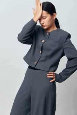 Gri elbiseli bir kadın. Elleri yüzünde. Yorgunluk ve hayal kırıklığını ifade ediyor. Tarafsız arka planda resmi kıyafetler giyen profesyonel bir kadın..