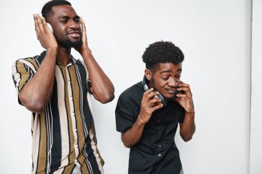 Siyah tenli genç adam kulaklıkla müzik dinliyor, beyaz stüdyo geçmişli günlük kıyafetlerle neşe ve dostluk ifade ediyorlar..