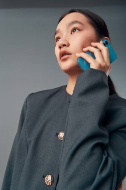 Profesyonel kıyafetli bir kadın konuşmak için cep telefonunu kullanıyor. Doğal makyajlı yakın plan portre, gösterişli saç stili ve iş ve kişisel iletişim için çağdaş tarz.