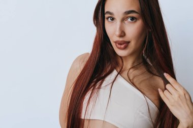 Kendine güveni tam genç bir kadın portresi. Uzun düz, kızıl saçlı, beyaz bluzlu. Önünde düz bir ışık var..