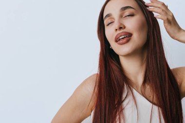 Düz kızıl saçlı, sakin ve gözleri kapalı bir kadın portresi. Beyaz bluzlu kadın model, arka planda güzellik, moda ve yaşam tarzı konsepti için el ele poz veriyor..