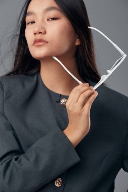 Gri arka planda beyaz gözlüklü, kendine güvenen genç bir kadının portresi. Koyu renk ceketli, uzun siyah saçlı ve yüzünde ciddi bir ifade olan bir kadın model..